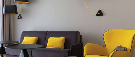 A modern living room with a grey sofa, two yellow chairs, a small round table, and two black lamps with yellow shades.