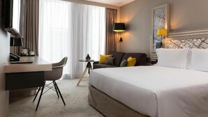 A hotel room with a large bed, a desk with a chair, a sofa, and a television. - Hilton Garden Inn Tours Centre (Tours)