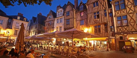 A historic European square with traditional half-timbered buildings, outdoor seating for cafes, and a cobblestone pavement.