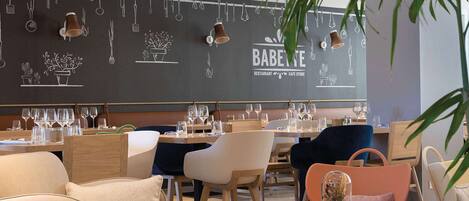 A modern restaurant interior with a blackboard wall displaying utensils and plants, wooden tables, and chairs.