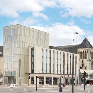 A modern building with a glass facade and a traditional building with a pointed roof in the background. - Hampton by Hilton Tours Centre (Tours)