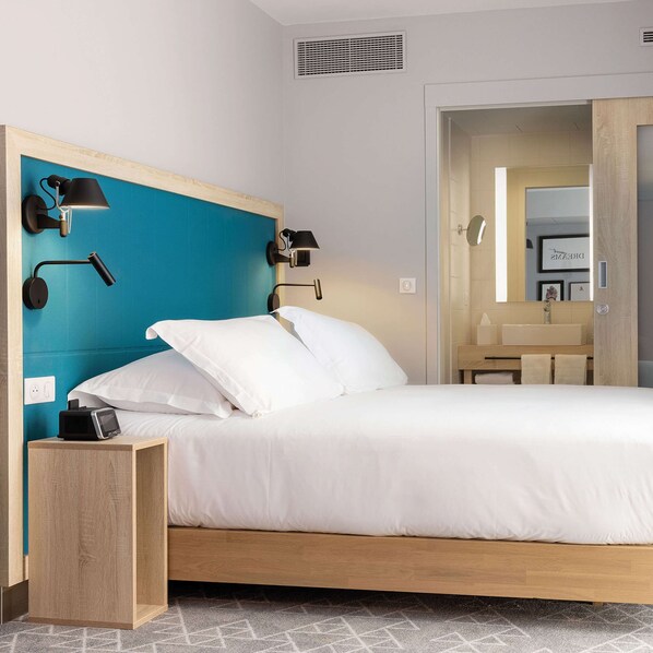A modern hotel room with a bed, bedside lamps, a nightstand, a bathroom visible through an open door, and a tiled floor. - Hampton by Hilton Tours Centre (Tours)