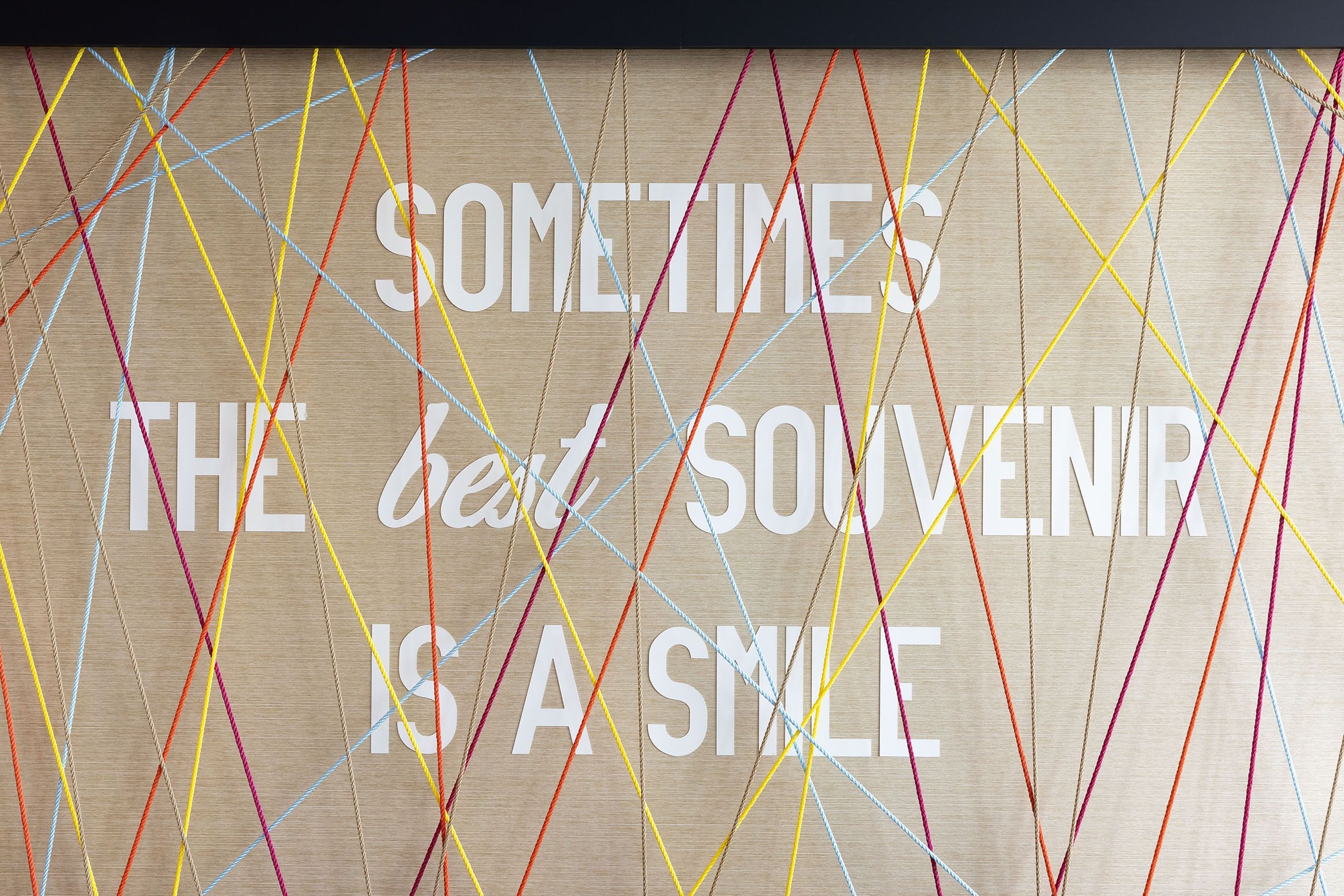 Una pared de madera con líneas de colores y el texto "SOMETIMES THE BEST SOUVENIR IS A SMILE".