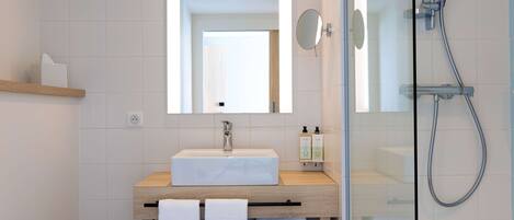 A modern bathroom with a glass-enclosed shower, a wooden vanity with a white sink, and a mirror above the sink.