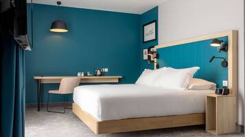 Une chambre d’hôtel moderne avec un mur d’accent de couleur turquoise, un cadre de lit en bois, un bureau avec une chaise et une table de chevet avec une lampe.