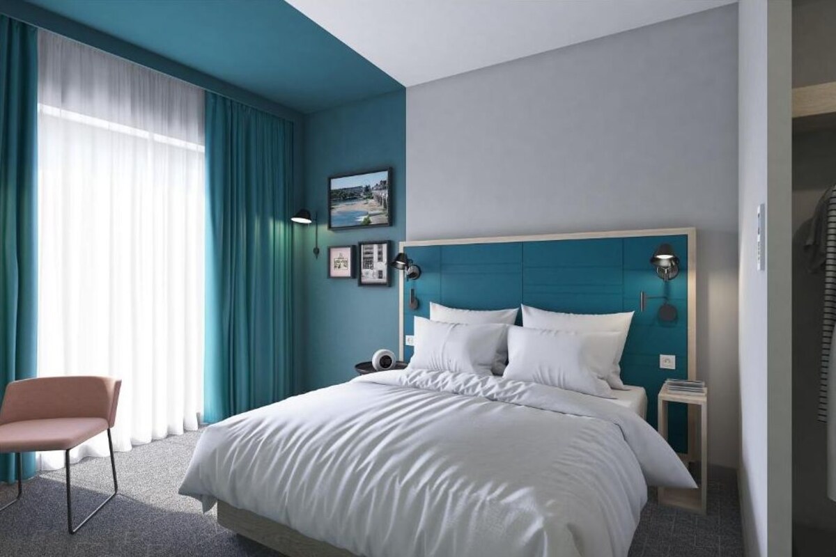Habitación de hotel con una cama grande, una silla, una mesita de noche y una ventana con cortinas.