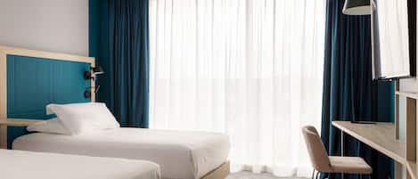 A hotel room with two beds, a desk, a chair, a TV, and a large window with curtains.