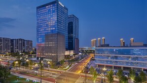A modern hotel with a glass facade, located in a cityscape with other high-rise buildings. - Hilton Yancheng (Yancheng)