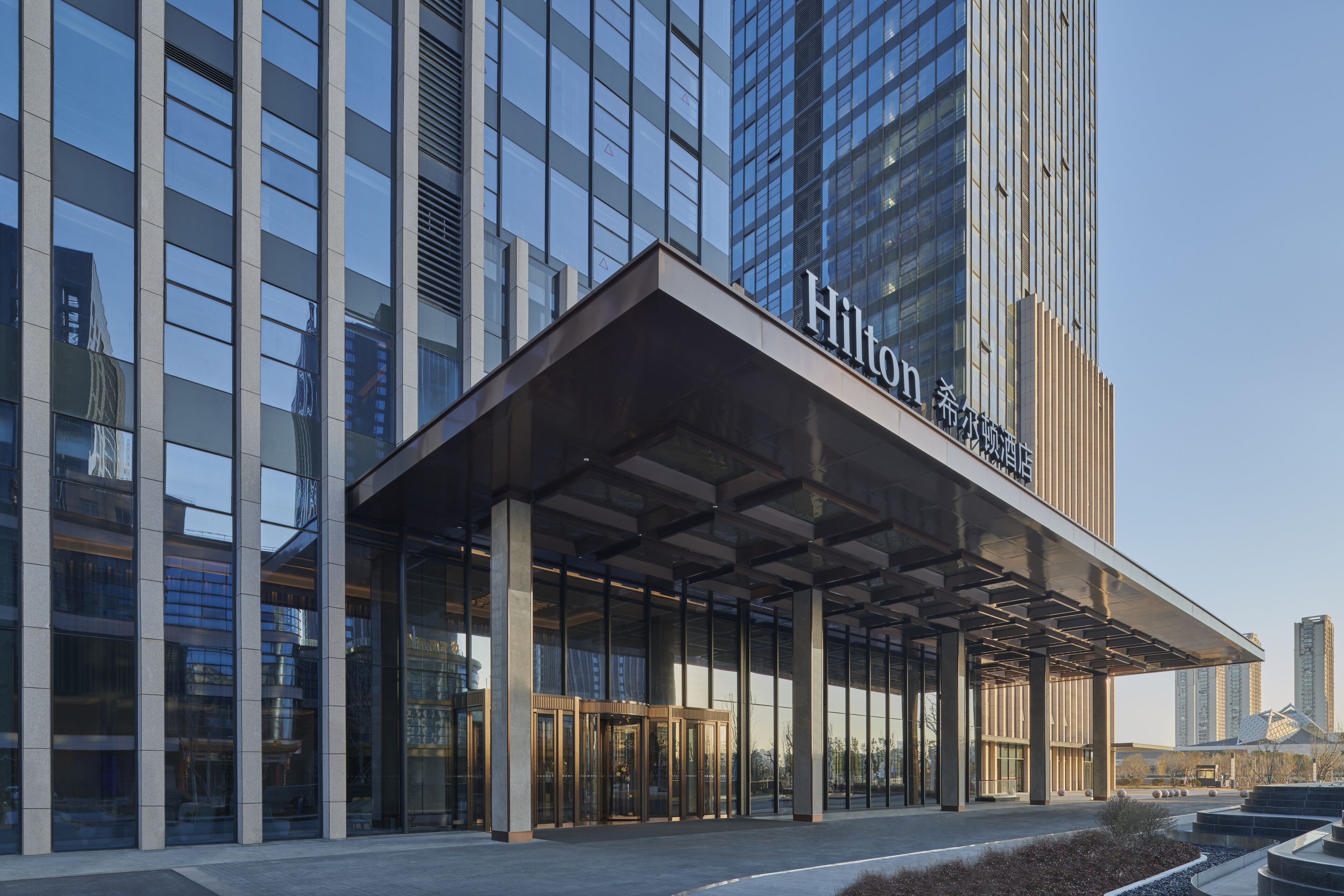 A modern hotel entrance with a glass facade, a covered entrance area, and a visible revolving door.