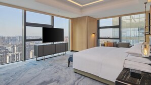 A modern hotel room with a large bed, a TV, a desk, and a view of a cityscape. - Hilton Yancheng (Yancheng)