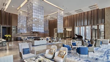 A spacious lobby with a grand piano, seating areas, and a bar.