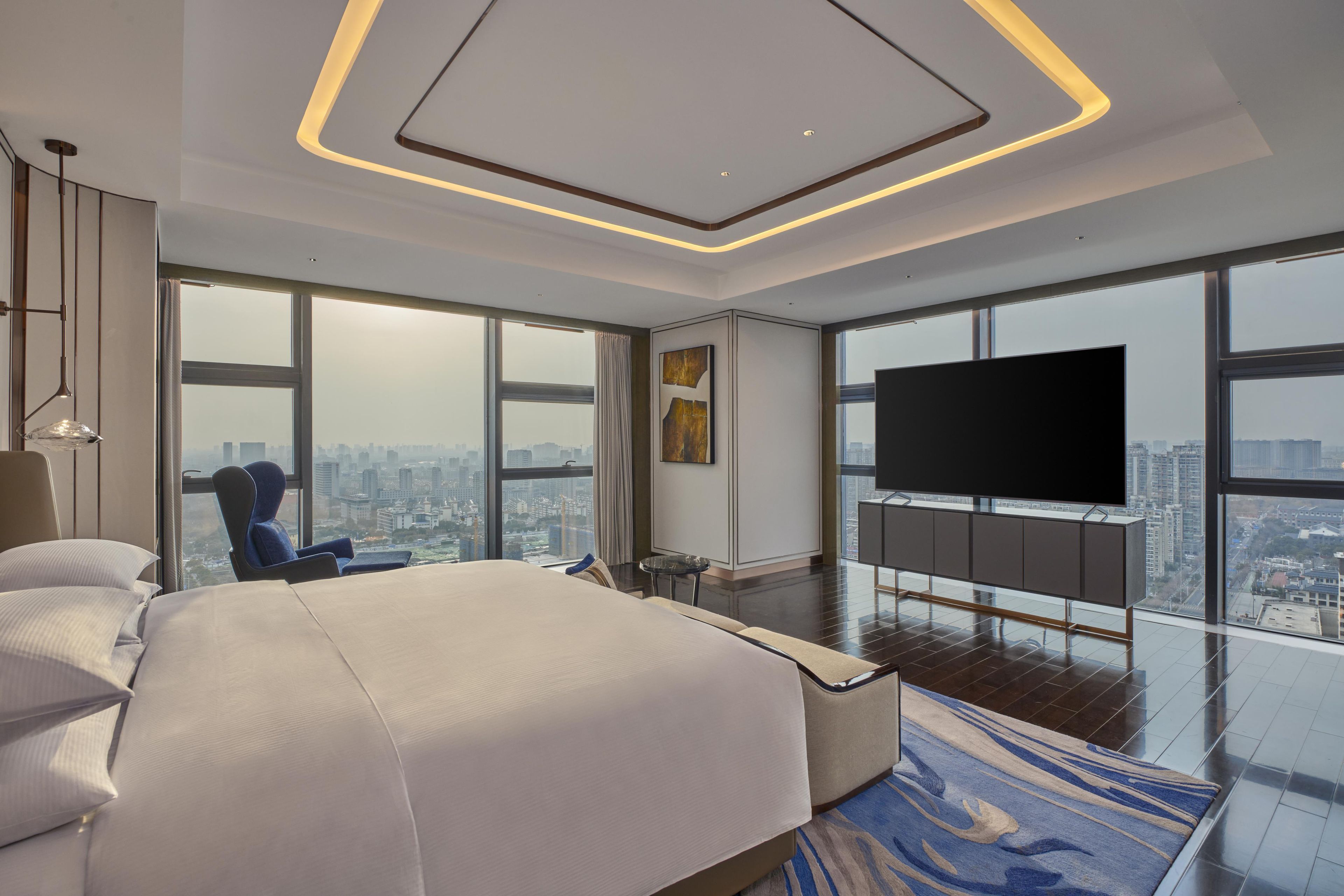 A modern hotel room with a large bed, a flat-screen TV, and a city view.