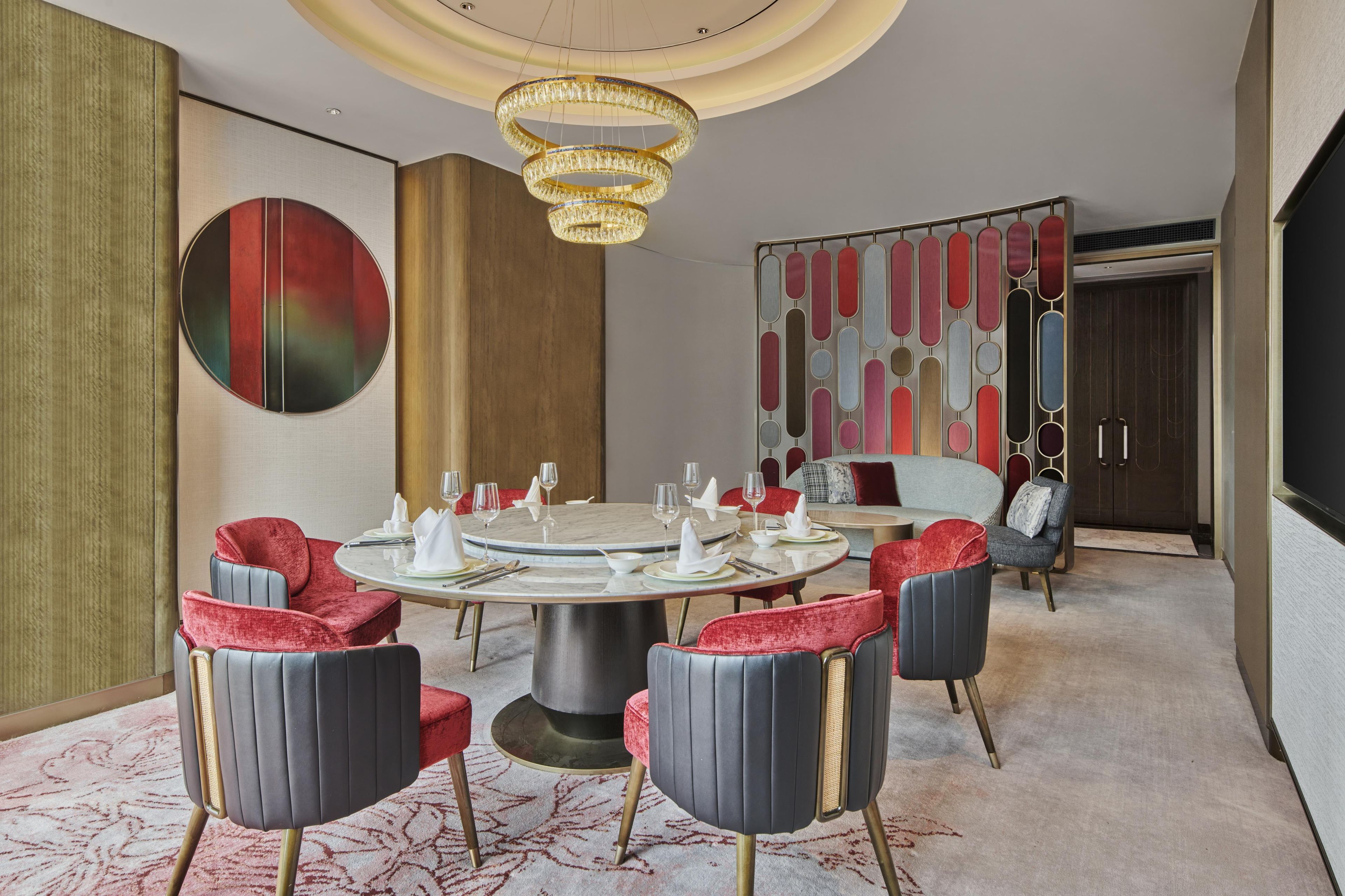 A dining area with a round table, red upholstered chairs, and a chandelier.