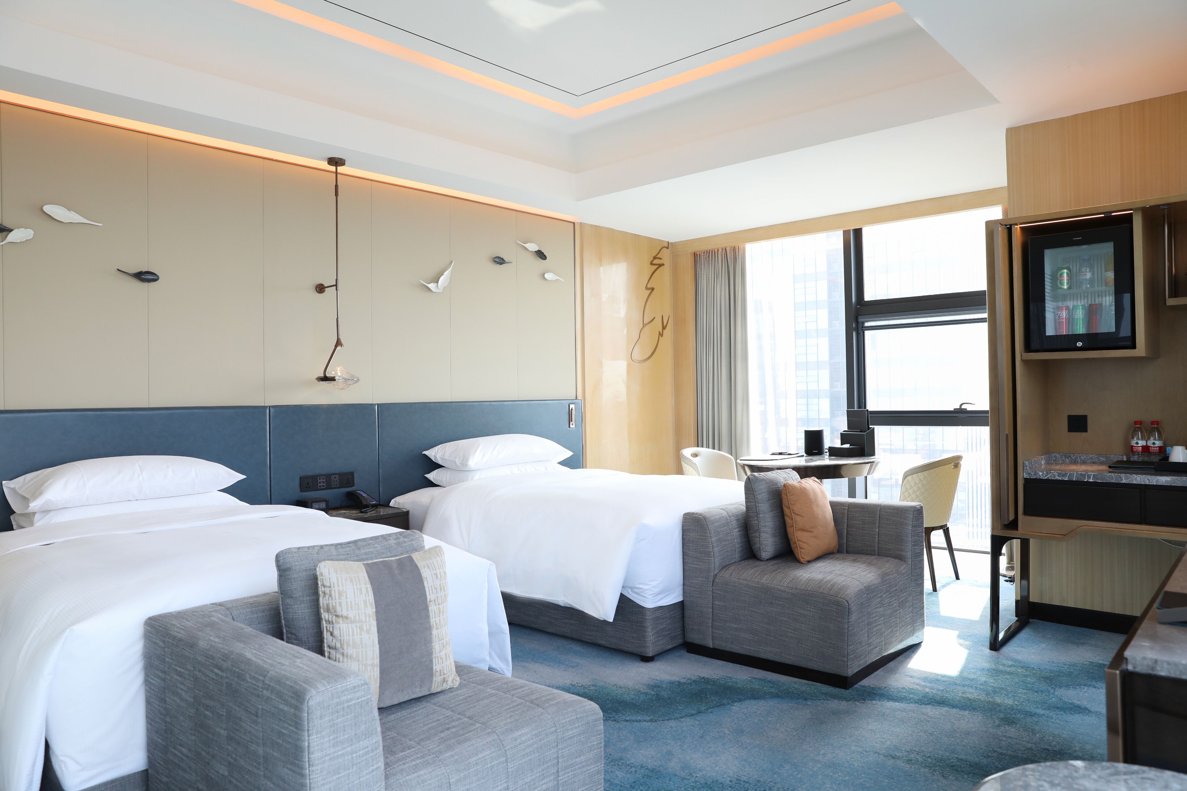 A hotel room with two beds, a sofa, a desk, a TV, and a large window.