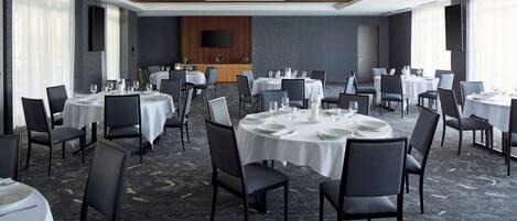 A conference room with round tables, chairs, and a large screen on the wall.