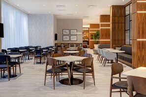 A modern dining area with multiple tables and chairs, a seating area with sofas, and a large potted plant. - Homewood Suites by Hilton Montreal Downtown, QC (Montreal)
