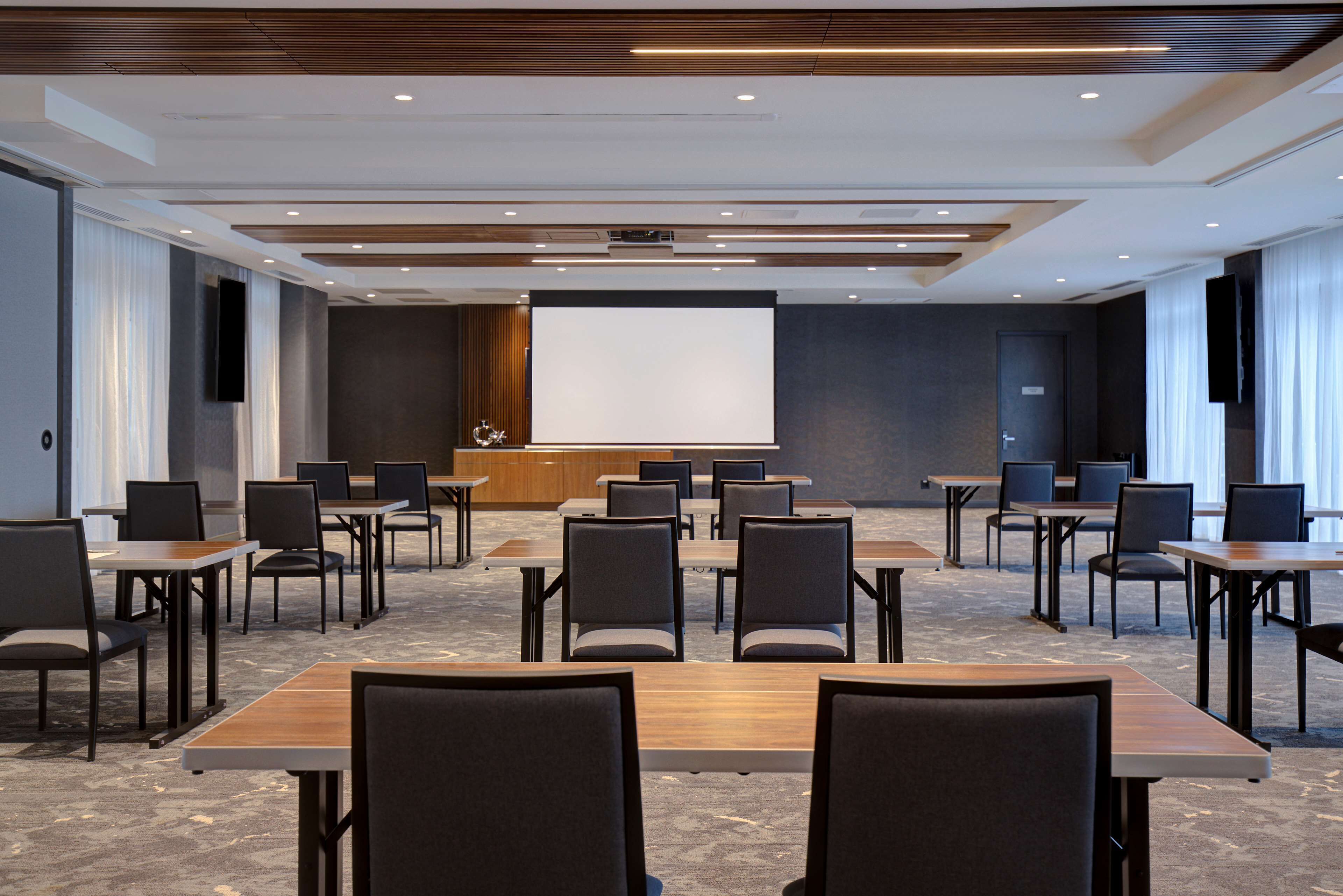 A conference room with a large screen, multiple tables, and chairs arranged for meetings.