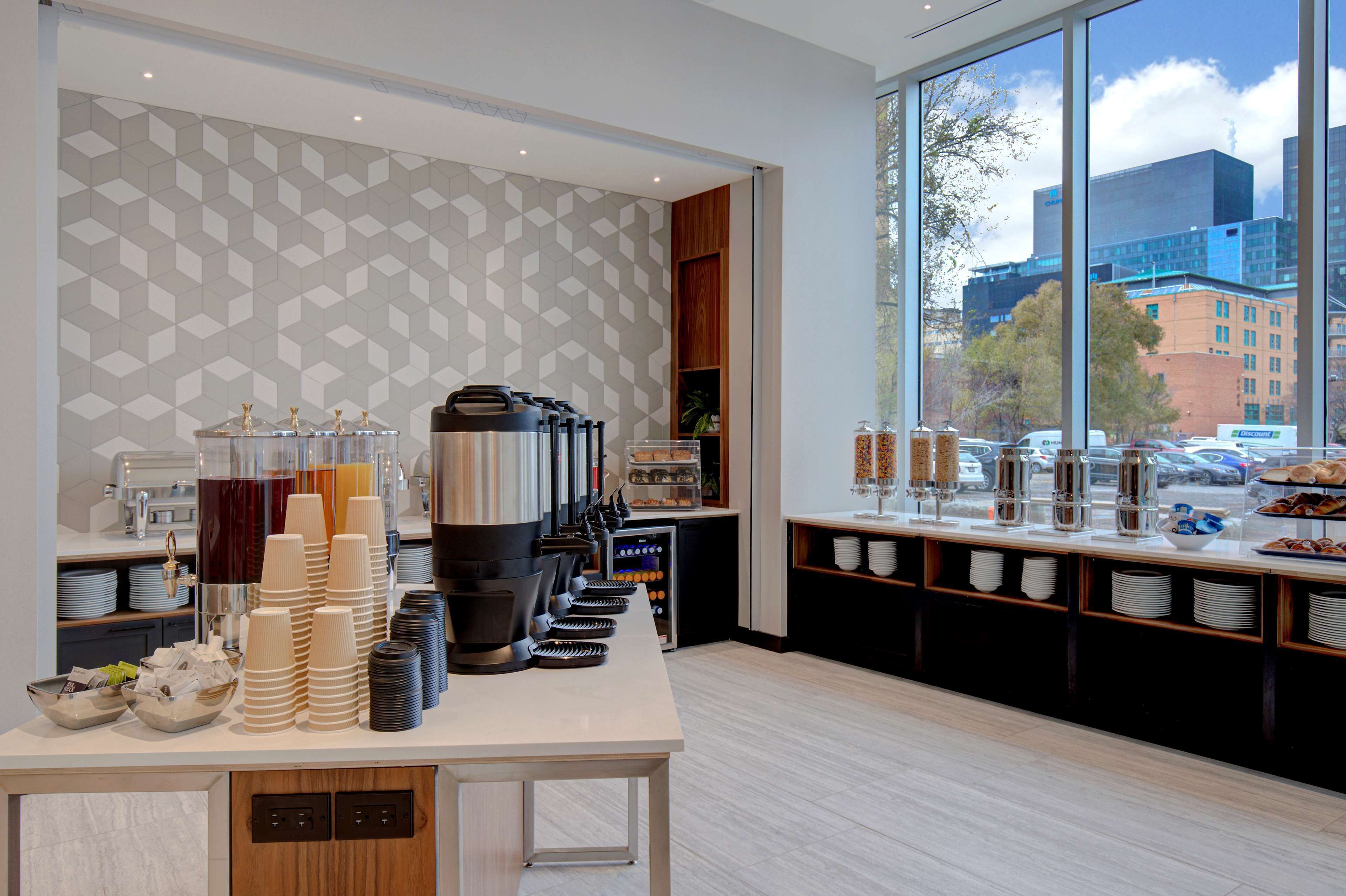 Una barra de desayuno moderna con una máquina de café, dispensadores de zumo y una variedad de productos para el desayuno.