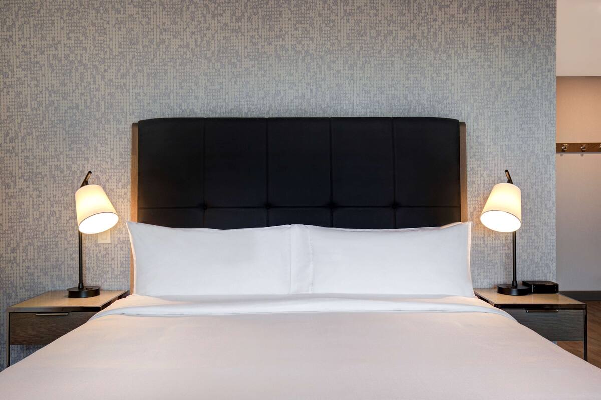 A neatly made bed with white linens, flanked by two bedside tables with lamps, set against a textured wall.