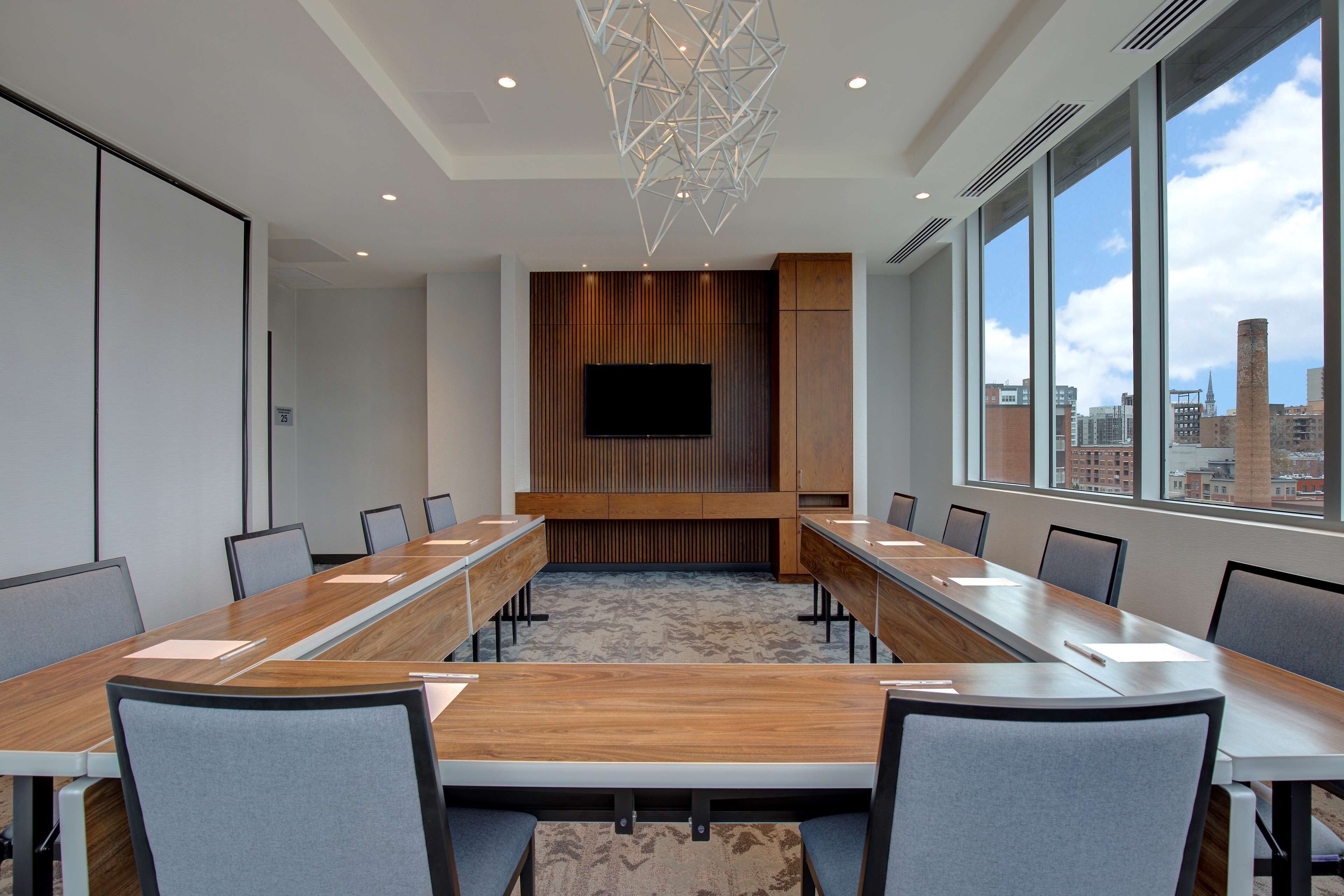 A conference room with a long table, chairs, a flat-screen TV, and a city view through large windows.