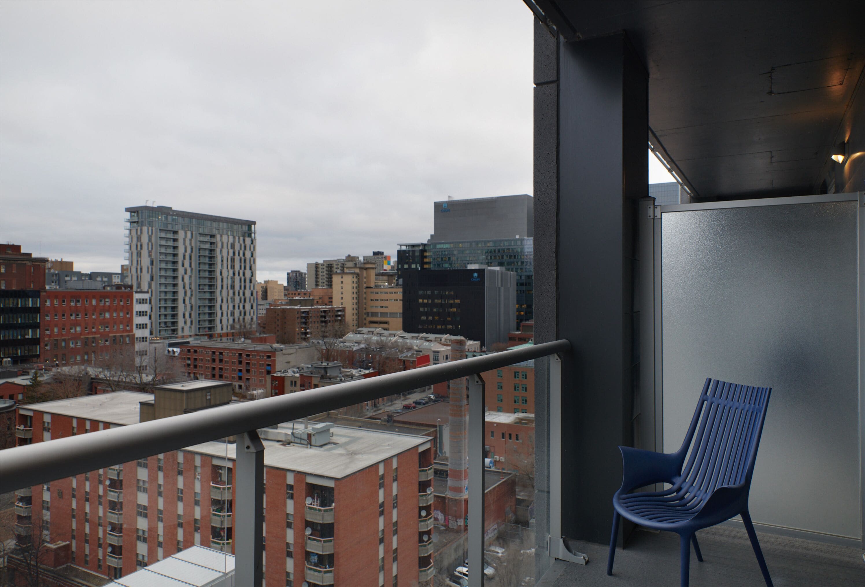 Un balcon avec une chaise bleue, donnant sur un paysage urbain composé de différents bâtiments.