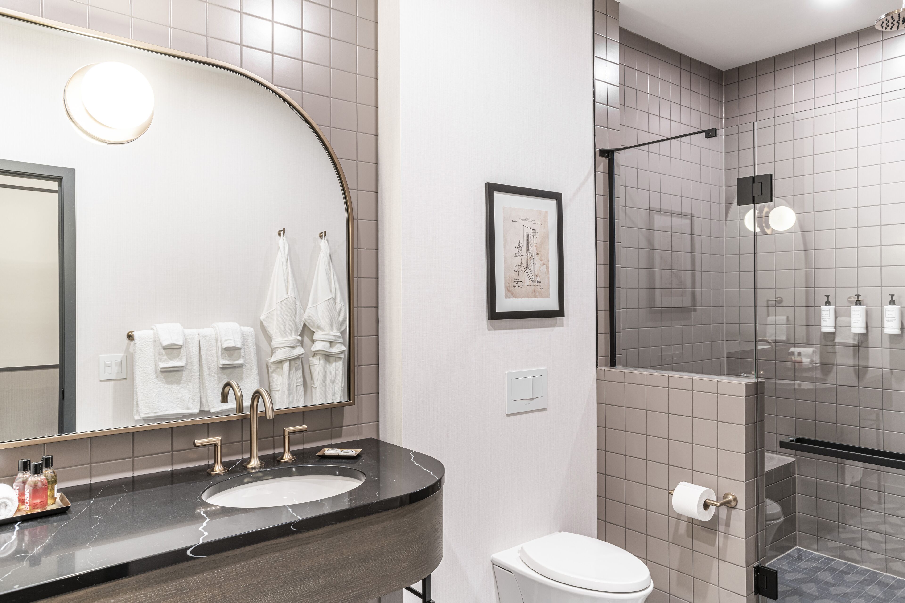 Un baño moderno con un espejo curvo, un lavamanos con encimera de mármol, inodoro y zona de ducha con puertas de cristal.