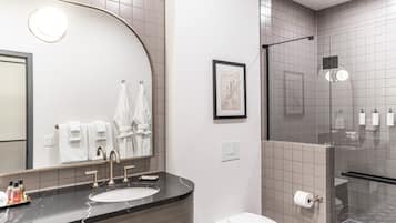 Un baño moderno con un espejo curvo, un lavamanos con encimera de mármol, inodoro y zona de ducha con puertas de cristal.