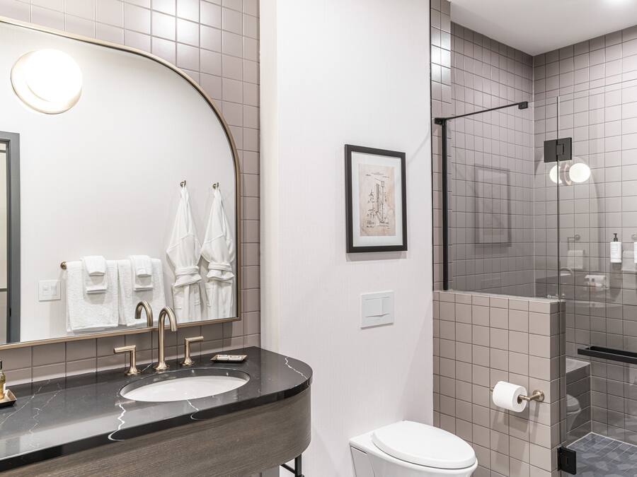 A modern bathroom with a curved mirror, a sink with a marble countertop, a toilet, and a shower area with glass doors.