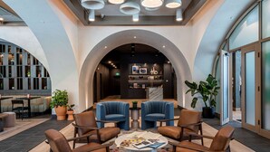 A modern lounge area with leather chairs, a central coffee table with magazines, and a bar area in the background. - The Westley Hotel - Tapestry Collection by Hilton (Calgary)