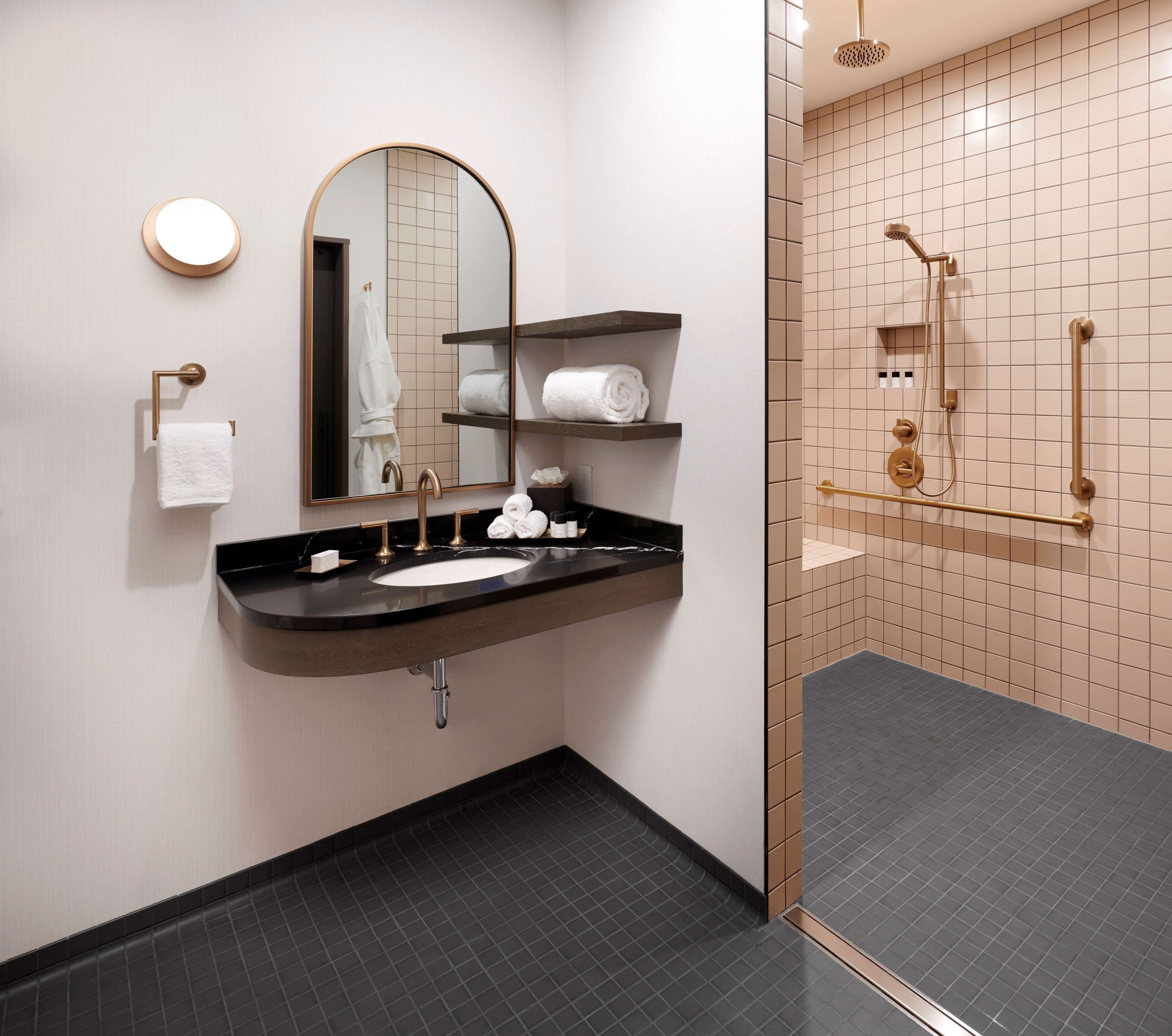A modern bathroom with a black sink, gold fixtures, a large mirror, and a walk-in shower with grab bars.