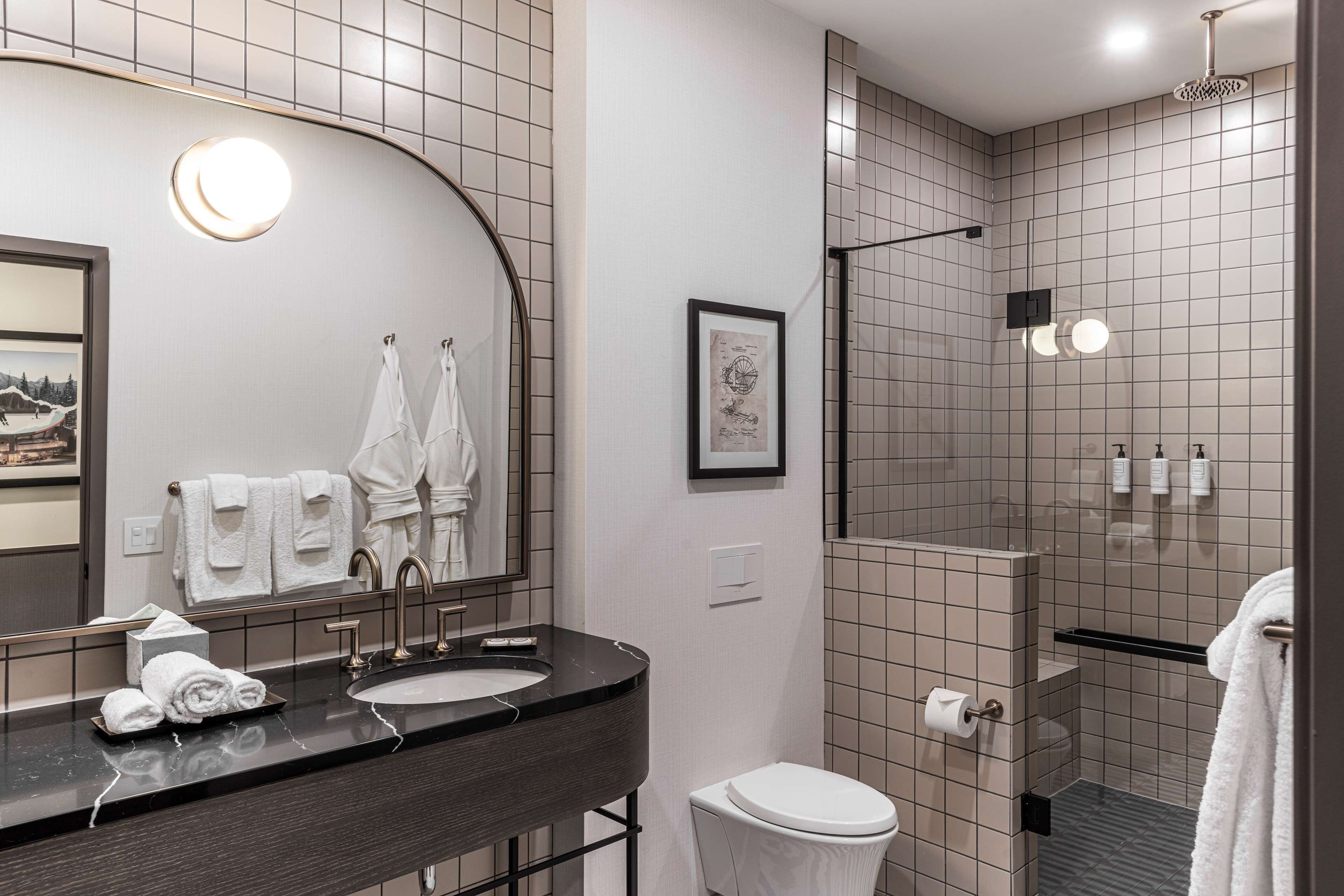 A modern bathroom with a large mirror, a sink, a toilet, and a shower area.