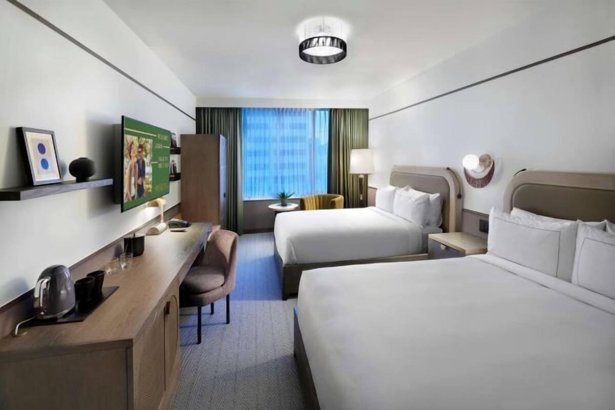 A hotel room with two beds, a desk, a chair, a TV, and a window with curtains.