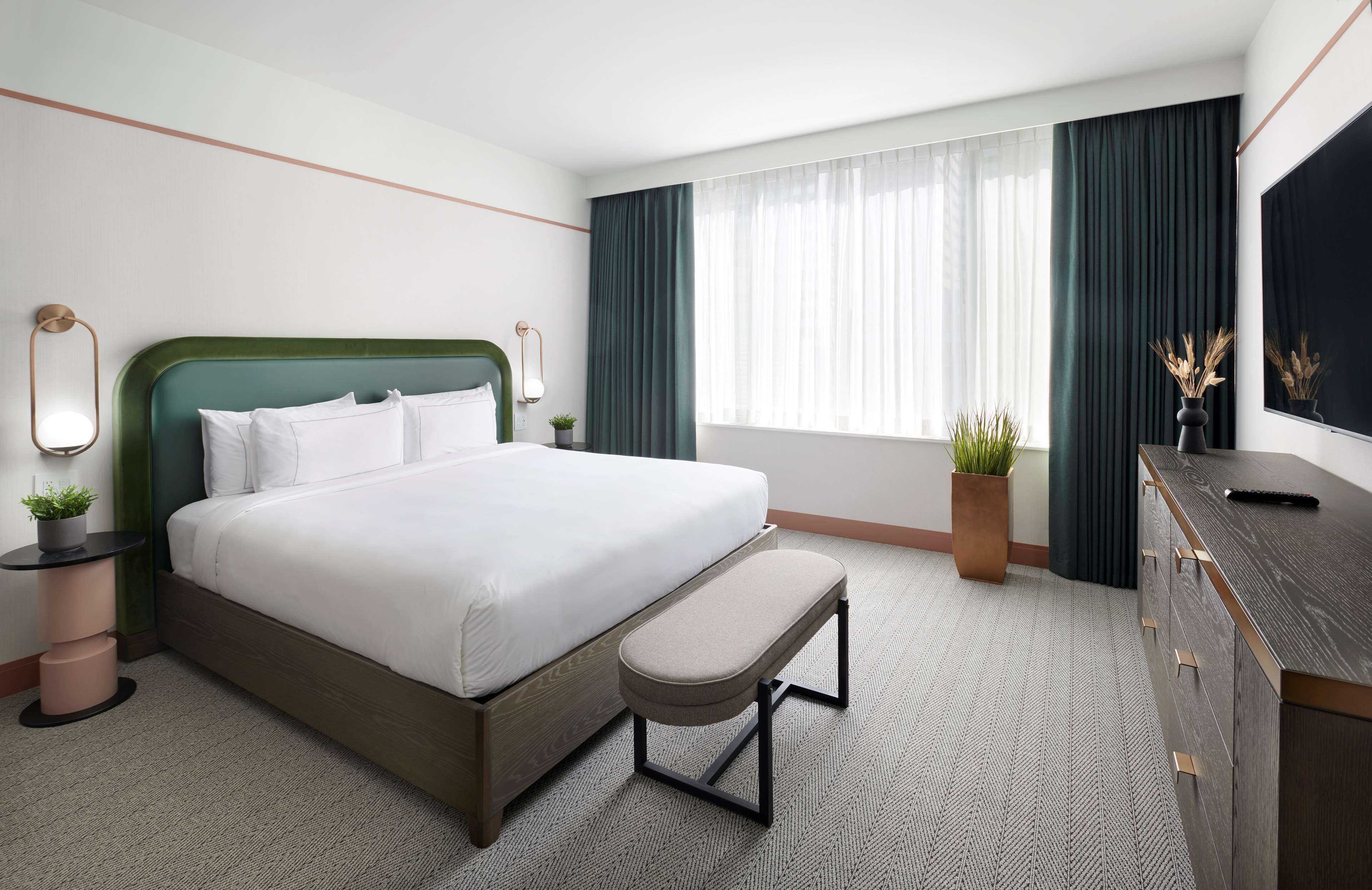 A hotel room with a bed, a bench, a dresser, and a TV.