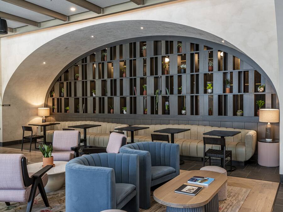 A modern lounge area with seating, tables, and a large arched wall with plants.