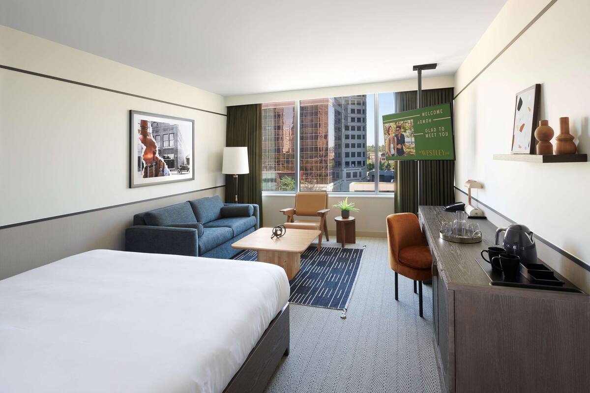 A hotel room with a bed, a sofa, a desk, and a view of the city.