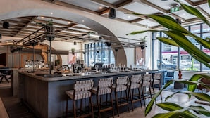 A modern bar area with a central island, bar stools, and a view of the city through large windows. - The Westley Hotel - Tapestry Collection by Hilton (Calgary)