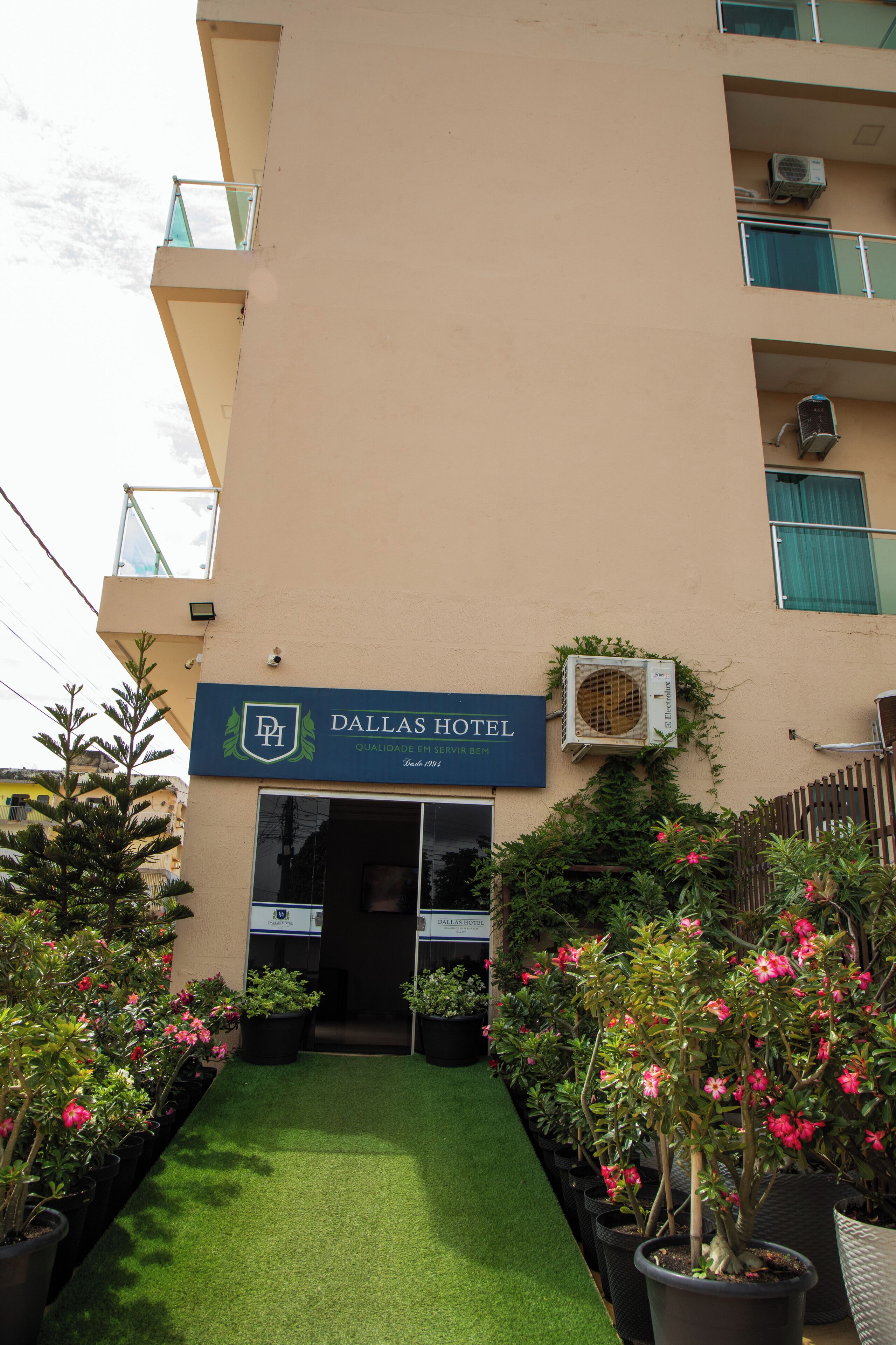 The exterior of the Dallas Hotel with a signboard, air conditioning units, and potted plants.