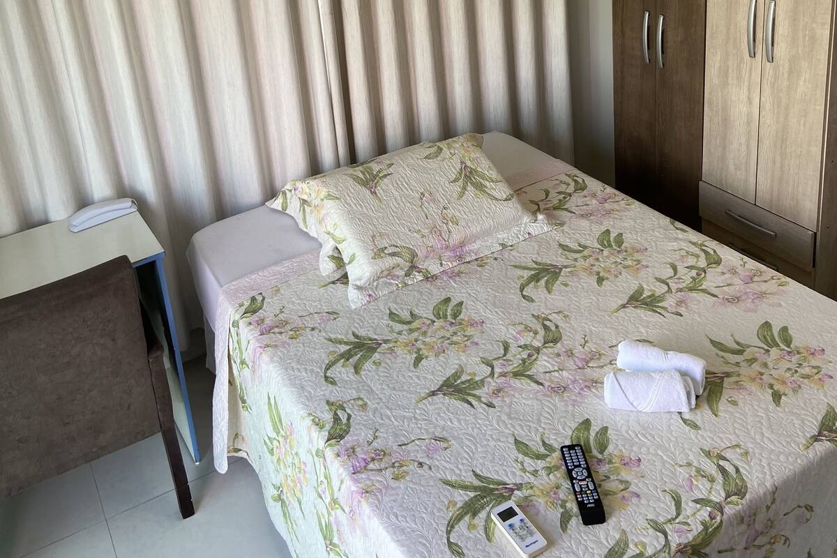 Ett hotellrum med en säng, ett skrivbord, en garderob och en gardin.