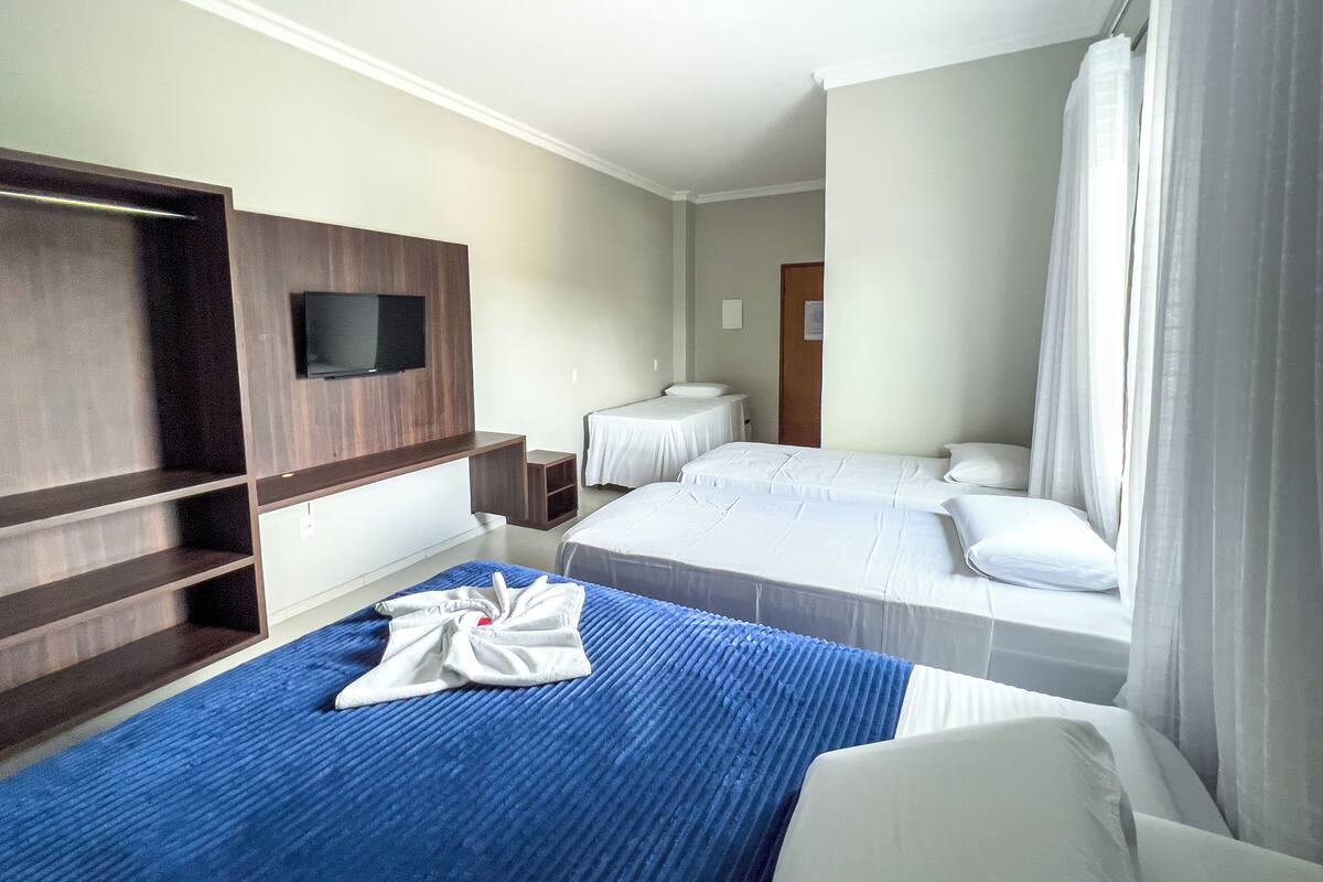 Ett hotellrum med en tv som är monterad på en vägg av trä, två sängar med vita sängkläder, ett blått, mönstrat överkast och en blå matta.
