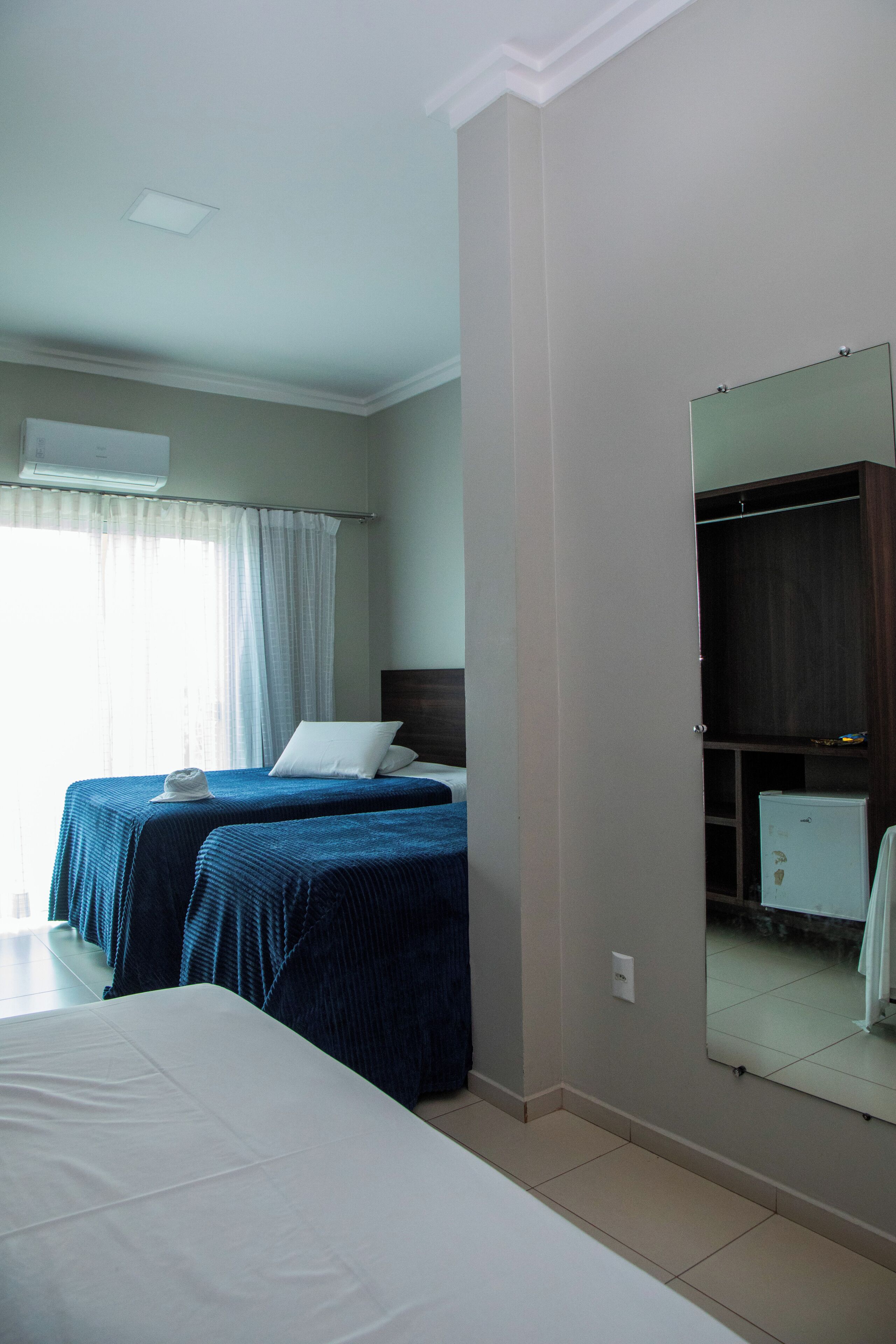 A bedroom with two beds, a wardrobe, a mirror, and a window with curtains.