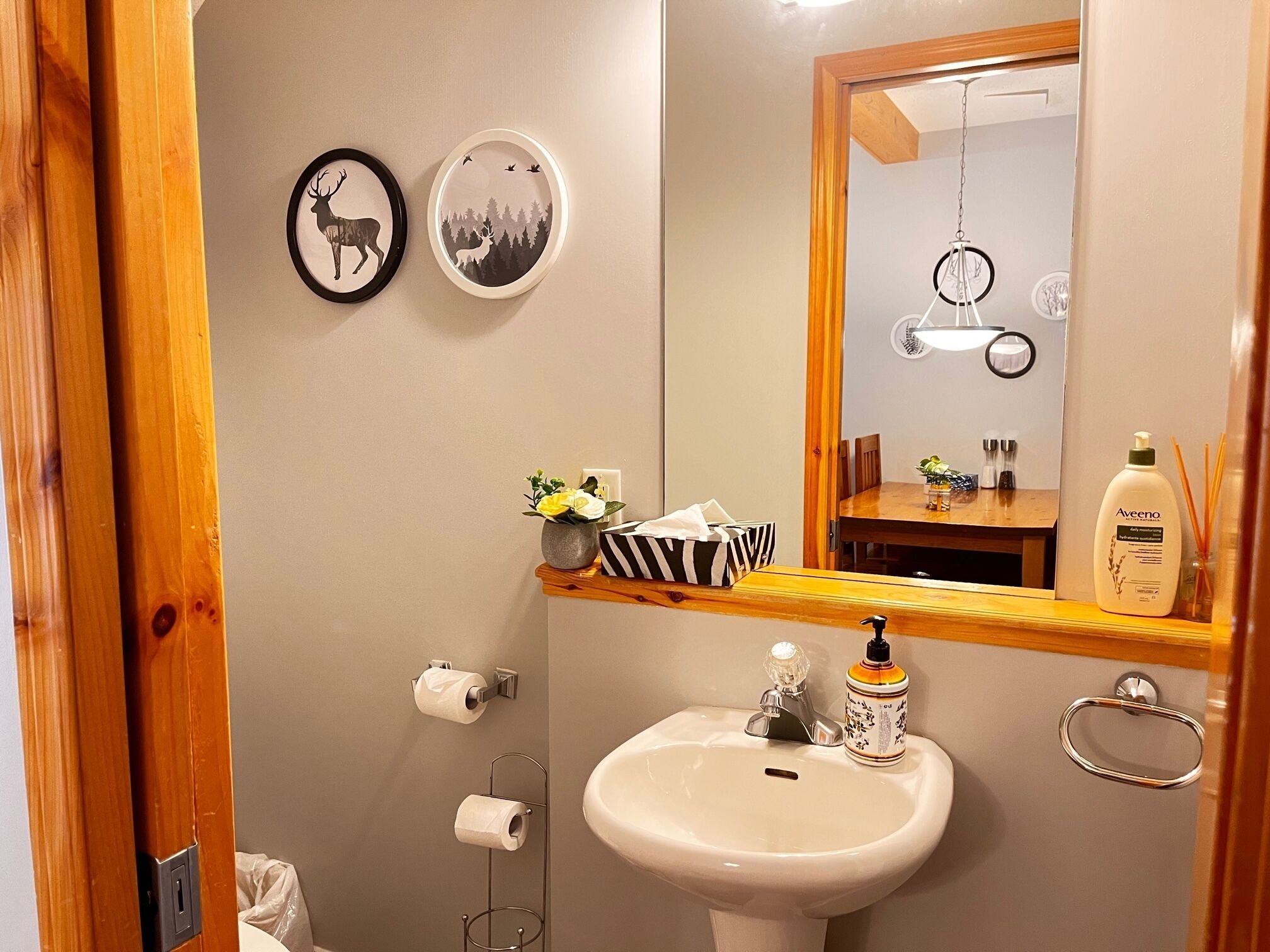 A bathroom with a sink, toilet paper, a mirror, and framed pictures on the wall.
