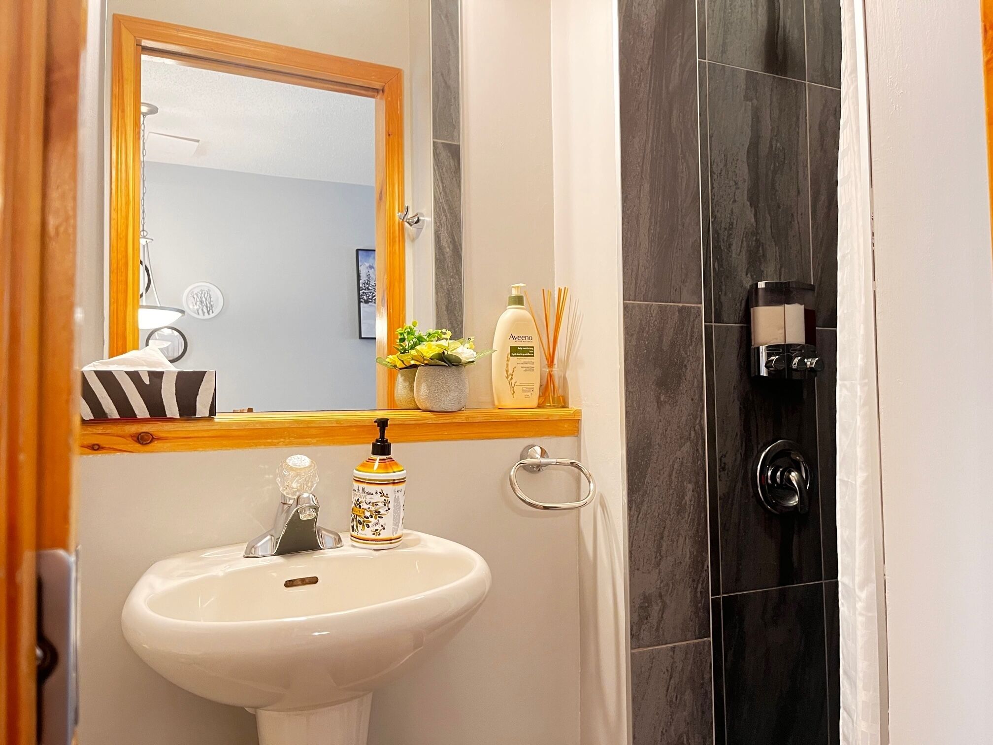 Een badkamer met een wit wastafelmeubel, een spiegel, een douche en toiletartikelen op een plank.