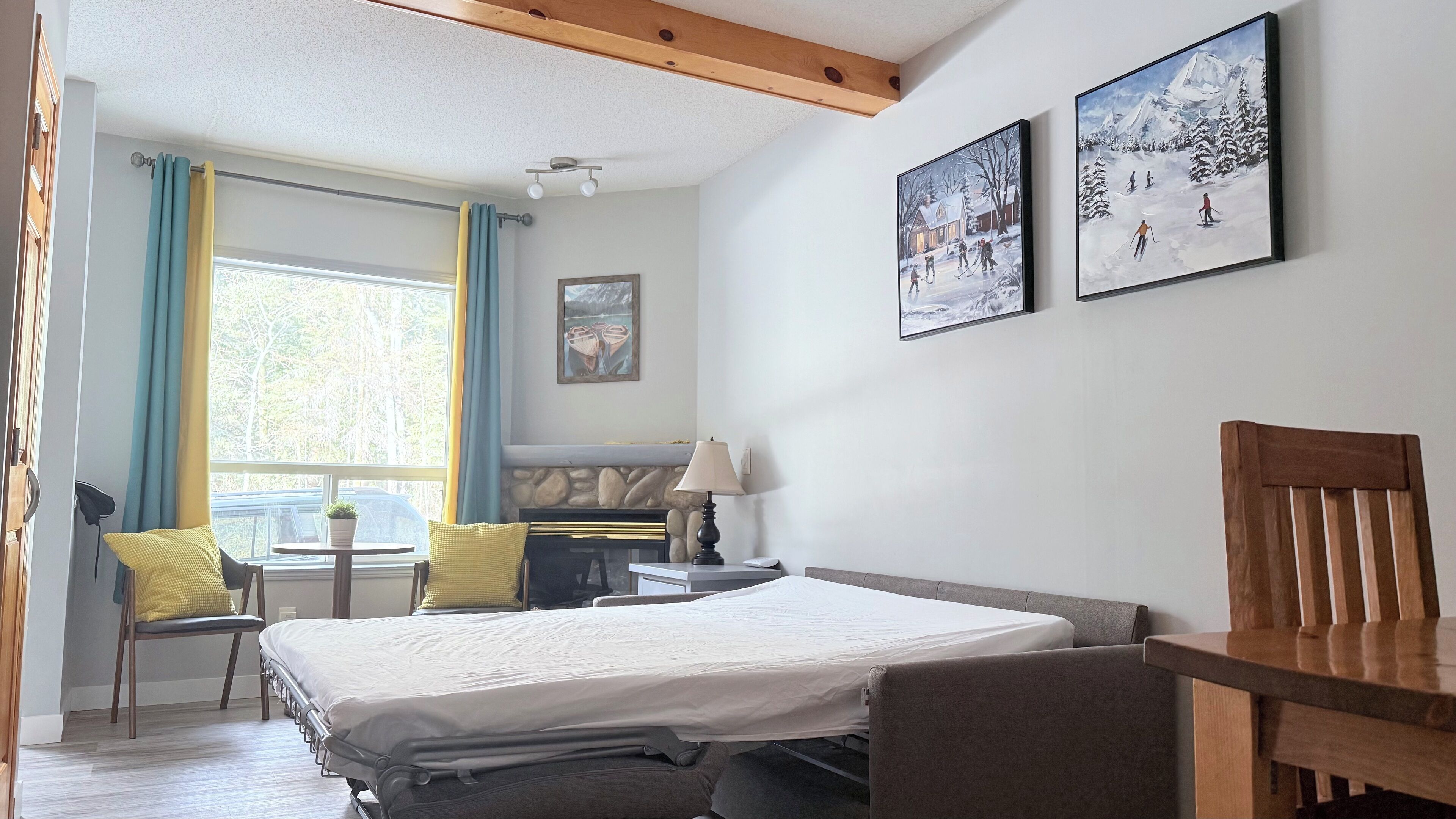 A hotel room with a bed, a desk, a chair, a lamp, and two paintings on the wall.