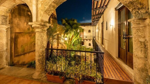 An outdoor corridor with stone arches, a wooden deck, and potted plants. - El Beaterio (Santo Domingo)