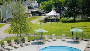 A swimming pool with lounge chairs and umbrellas, surrounded by a grassy area and a mountain backdrop.