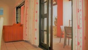 Ein Zimmer mit einer Couch, einem Sessel, einem Tisch und einem Vorhangfenster.