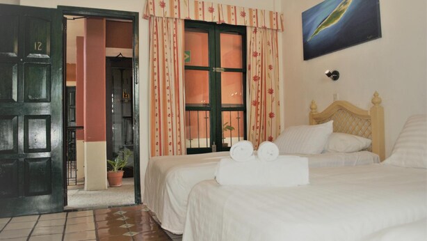 Ein Hotelzimmer mit zwei Betten, einem Holzkopfende, einem Blumentopf und einem Bild an der Wand.