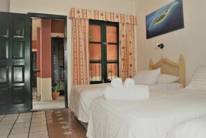 A hotel room with two beds, a wooden headboard, a potted plant, and a painting on the wall.