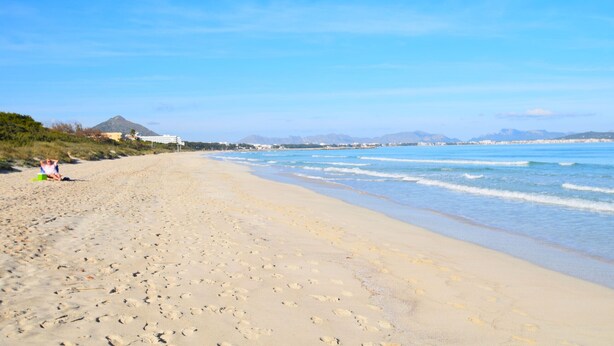 A wide sandy beach with footprints leading to the water, a clear sky, and distant mountains. - Es Camp Pla 087 cosy finca with private pool, terrace, garden, barbecue and air-conditioning (Sineu)