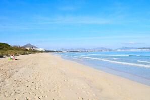 A wide sandy beach with footprints leading to the water, a clear sky, and distant mountains.